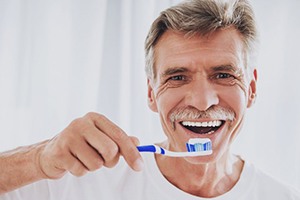 older man in white t-shirt brushing his teeth 