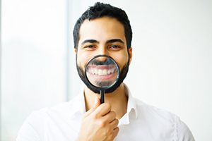 man holding magnifying glass to smile to show off dental crowns in South Portland 