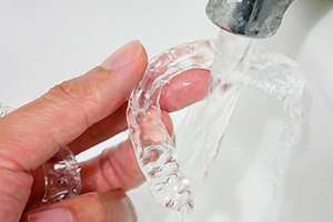 Patient rinsing clear aligner with water in sink