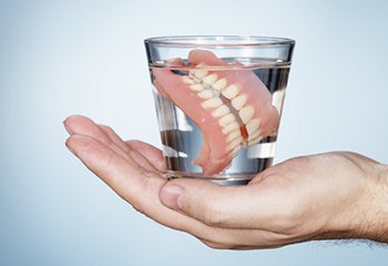 hand holding full dentures in glass of water