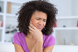 woman in purple shirt with toothache who needs emergency dentist