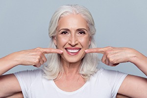 woman with dental implants pointing to her smile