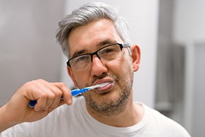 man with glasses brushing his teeth