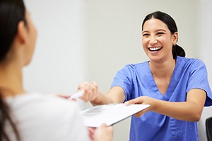 Front desk woman at dentist smiling at patient with clipboard